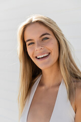 A young, beautiful blonde woman in Miami Beach, wearing a white top, smiles warmly at the camera.