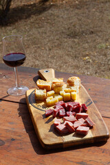 Tabala de madera con un aperitivo junto a una copa de vino tinto al aire libre. Vista superior y de...