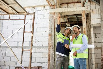 workers or architects working on tablet and pointing up to something at construction site