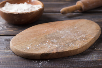 Wooden cutting board sprinkled with flour, wooden bowl with flour and rolling pin for cooking on...