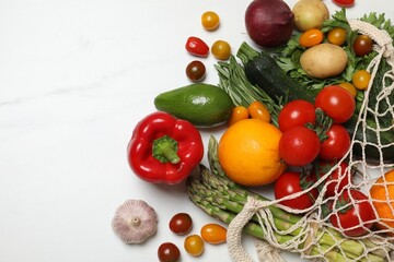 Vegan food delivery. Net bag with different fresh vegetables and fruits on white marble background, flat lay. Space for text
