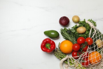Vegan food delivery. Net bag with different fresh vegetables and fruits on white marble background, flat lay. Space for text