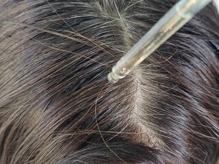 Woman applying essential oil onto hair on blurred background