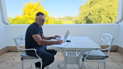 A man sits on a balcony, working on his laptop