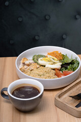 A bowl of couscous with meat, eggs and avocado, vegetables and a cup of coffee on the restaurant table