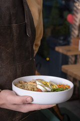 Bowl with dish in the hand of waiter in apron. Concept of healthy balanced nutrition, service area