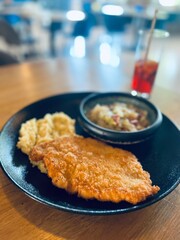 Breaded fish fillet served with mashed potatoes and tomato sauce on wooden table