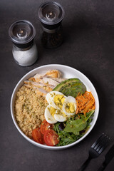 Plate with eggs, vegetables, couscous and meat on dark background top view