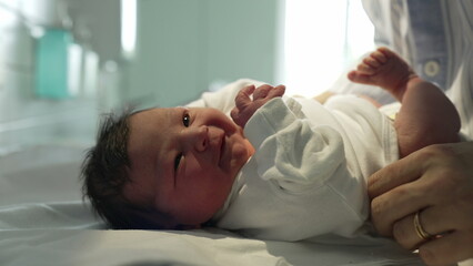 Obraz premium Newborn baby being gently dressed in a white onesie by caring hands in a hospital, showcasing the delicate and tender care given to newborns immediately after birth in a medical setting