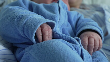 Newborn baby in a blue onesie resting in a parent's arms, emphasizing the tender and cozy moments of early bonding and the peacefulness of the baby's nap