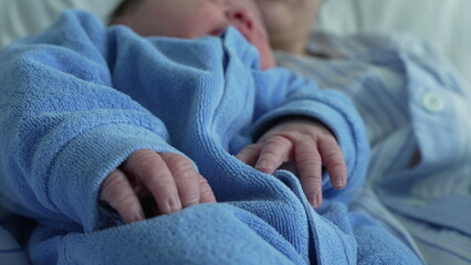 Newborn baby in a blue onesie resting in a parent's arms, emphasizing the tender and cozy moments of early bonding and the peacefulness of the baby's nap