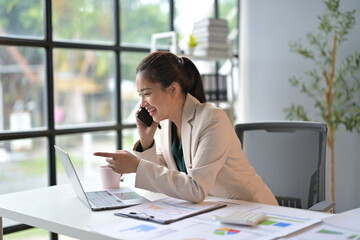 Businesswoman is working in her bright and modern office. She is multitasking, talking on the phone and pointing at her laptop screen