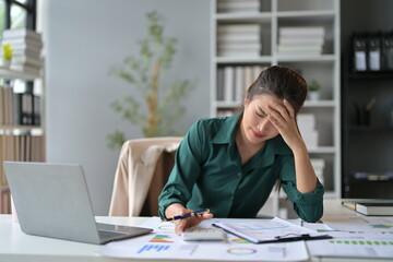 Young asian businesswoman is having a headache and feeling tired from working on a laptop computer at her office desk