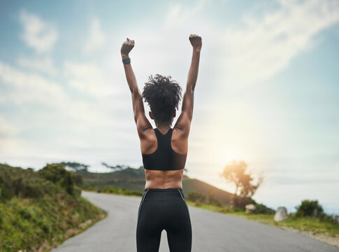 Woman, runner and winner or back in road, celebration and arm for achievement or fitness or body goals. Outside, marathon training and cardio exercise with athlete, first pump and proud wellness