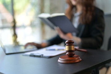 Lawyer working on a laptop while reading a law book, with a judge's gavel on the desk, exuding...