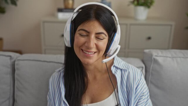 Young beautiful brunette hispanic woman wearing a headset smiling in a cozy living room at home