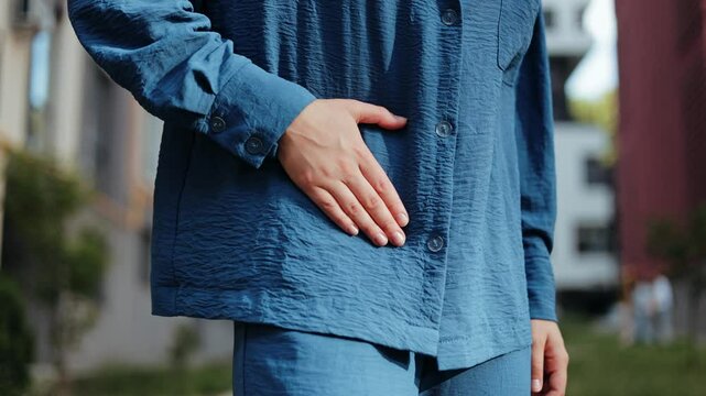 A young woman experiencing severe abdominal pain outdoors. Could be a medical or health concept.