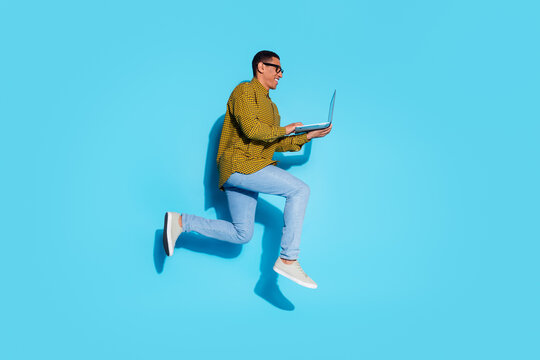 Full length photo of handsome young guy running hold netbook dressed stylish plaid garment isolated on blue color background
