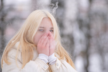 Portrait of a young beautiful blonde girl outdoors in winter in cloudy weather.