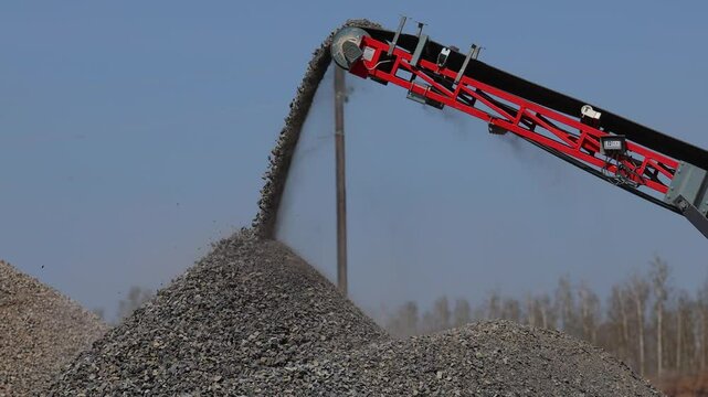 Production of crushed stone. Heavy machinery for crushing stone. Extraction of stone in a quarry. Crushed stone falls from a conveyor belt.