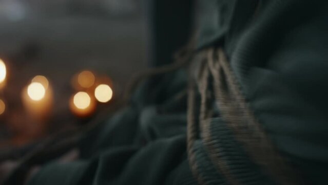 Side closeup of chest and arms of unrecognizable devil possessed person in velour jacket writhing on chair while being tied up with rope and trying to break free indoors