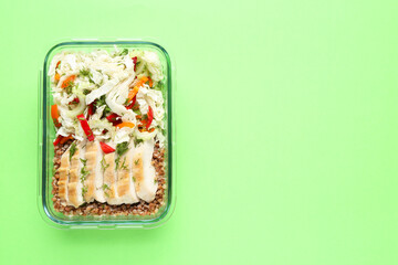 Healthy meal. Fresh salad, chicken and buckwheat in glass container on green background, top view. Space for text
