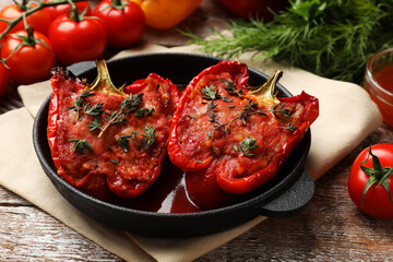 Tasty stuffed peppers in dish and ingredients on wooden table