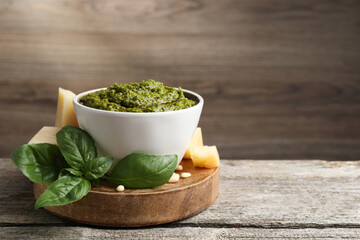 Tasty pesto sauce in bowl, basil, cheese and pine nuts on wooden table, space for text