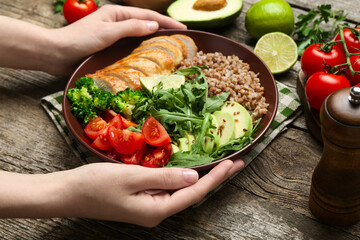 Healthy meal. Woman with tasty products in bowl at wooden table, closeup