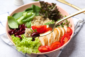 Healthy meal. Eating tasty vegetables, quinoa and chicken breast with fork from bowl on white table, closeup