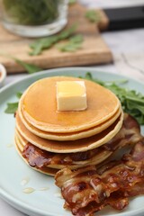 Tasty pancakes with butter, fried bacon and fresh arugula on white marble table, closeup