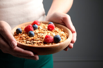 Woman holding bowl of tasty granola with berries and nuts on dark grey background, closeup