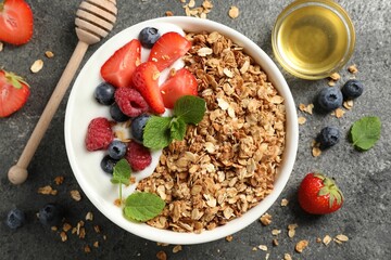 Tasty granola with berries, yogurt and honey on grey textured table, flat lay