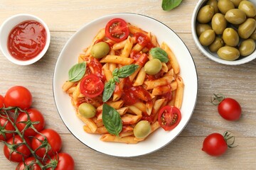 Delicious pasta with tomato sauce, basil and olives in bowl on wooden table, flat lay