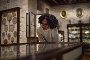 Thoughtful young woman wearing glasses and looking at exhibition. Concept of Museum Day