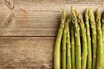 Fresh green asparagus stems on wooden table, flat lay. Space for text