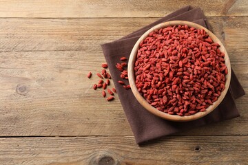 Dried goji berries in bowl on wooden table, top view. Space for text