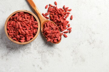 Dried goji berries, bowl and spoon on grey textured table, flat lay. Space for text