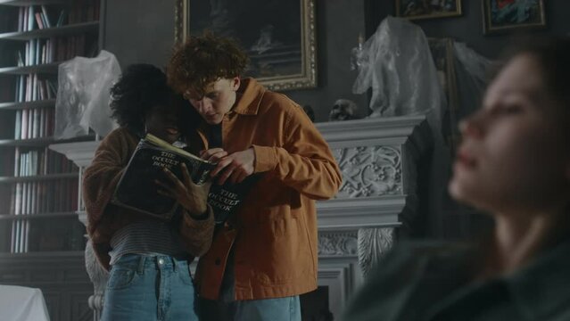 Medium long shot of diverse adolescents seeking prayers in Latin in occult book to perform exorcism rites on their writhing demon obsessed girl friend who tied up with rope to chair in old house