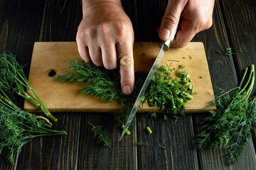Chopping dill with a knife on a cutting board. A cook prepares dill or fennel for canning.