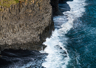 Aerial view of basalt columns and crashing waves at Reynisfjara black sand beach, Iceland.