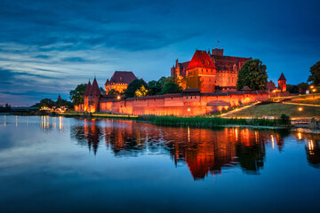 Castle of theTeutonic Order in Malbork by the Nogat river at night with full moon.