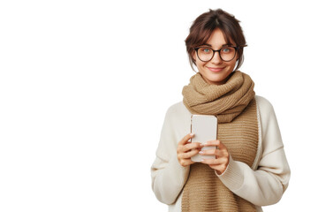 Smiling woman with glasses holding a smartphone, wearing a cozy scarf and sweater, isolated on a white background.