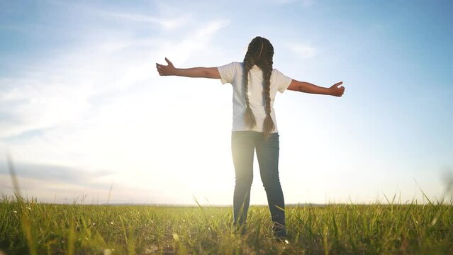 The free child's arms are looking to the sky. Religion freedom unity with nature concept. Girl in nature and religion with the sun. Girl child praying hands to sides looking lifestyle up in nature.