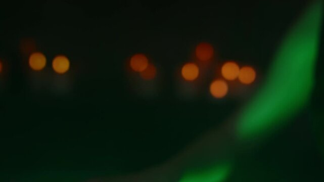 Side tilt closeup of young attractive witch with big black eyes casting spell and making poisonous potion in pot at night, illuminated by green light