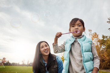 Mom, daughter and blowing bubbles in park with smile for fun, playing and bonding with child...
