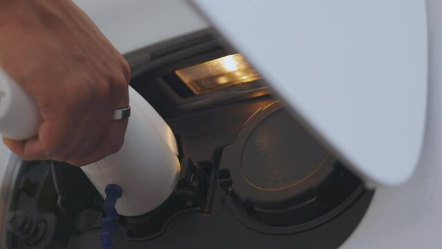 Close-up of hand plugging off charger from electric vehicle (EV), and ready to go. It shows sustainability, green technology, renewable energy, environmental conservation, and zero-emission vehicles. 