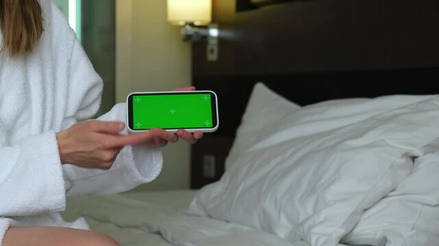 A woman in a bathrobe is sitting on the bed. Women's hands will scroll the phone. 4k video. High quality 4k footage