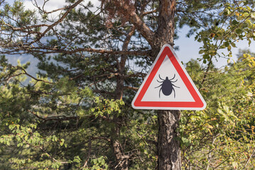 Tick parasite warning sign on the tree at a forest enter, in the mountain landscape. Risk, danger, and Lyme disease concept.