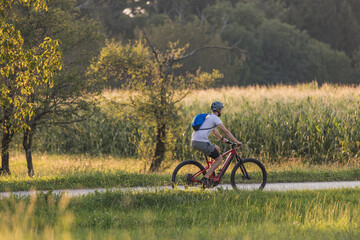 Man biking electric mountain bike along the trail in a fantastic rural landscape at sunset